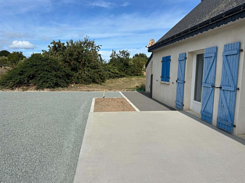 Terrasse béton et cour en gravillon devant une maison aux volets bleus