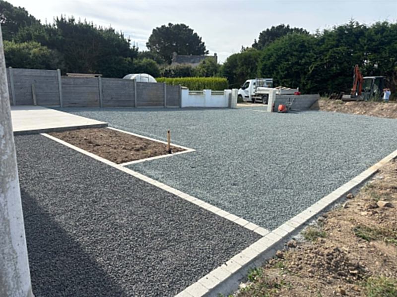 Cour gravillonnée délimitée par des bordures béton et des espaces plantés