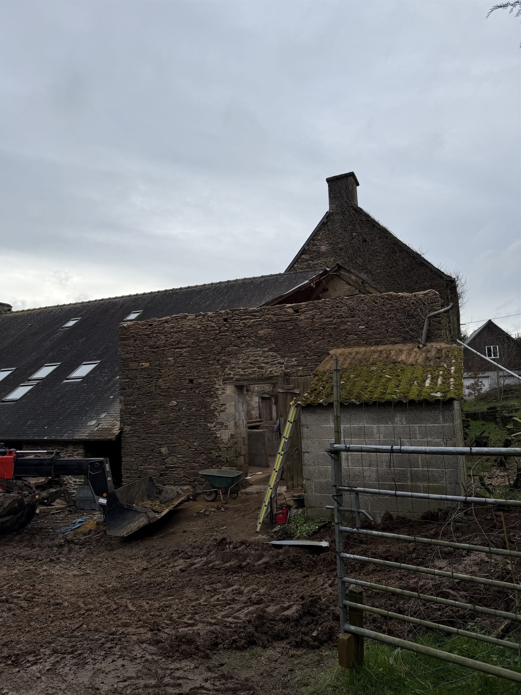 Bâtiment en pierre en cours de démolition, brouette et godet de pelle