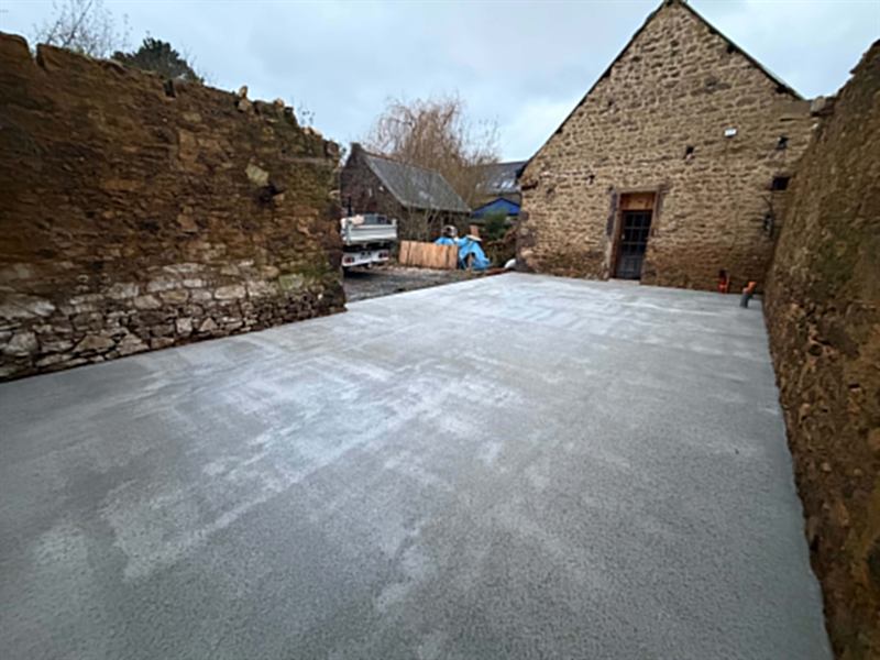 Grande dalle béton talochée dans une cour entourée de bâtiments en pierre