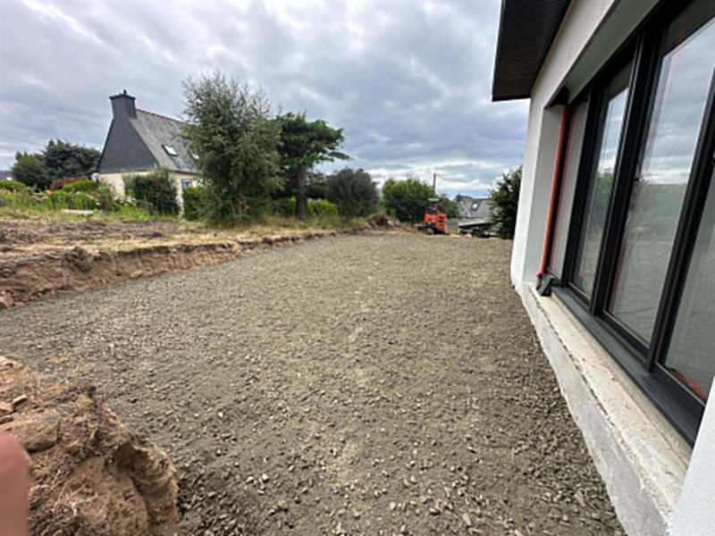 Plateforme empierrée le long d'une maison neuve, mini-pelle au fond