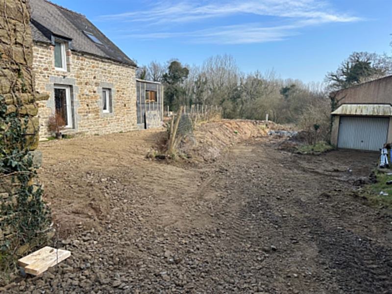 Cour terrassée devant une longère en pierre, talus profilé
