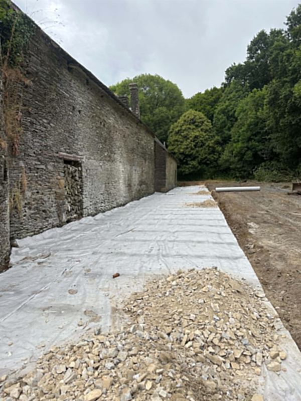 Géotextile déroulé le long d'un bâtiment en pierre avant empierrement