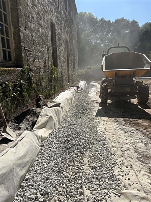 Apport de gravier au dumper le long d'un mur en pierre