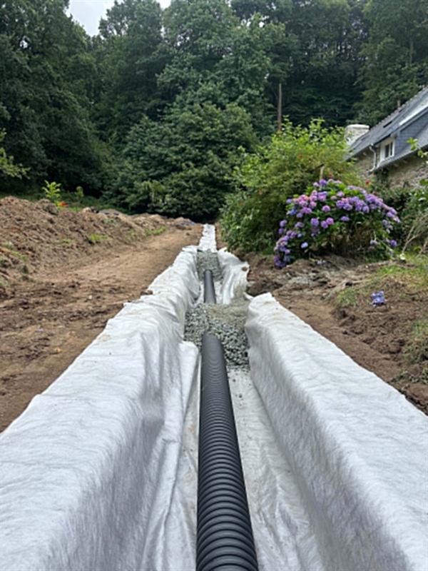 Drain posé sur lit de gravier dans une tranchée doublée de géotextile