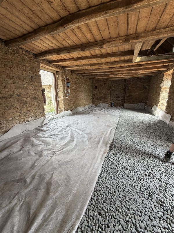 Intérieur en pierre à plafond de poutres bois, sol recouvert de pierres concassées sur géotextile