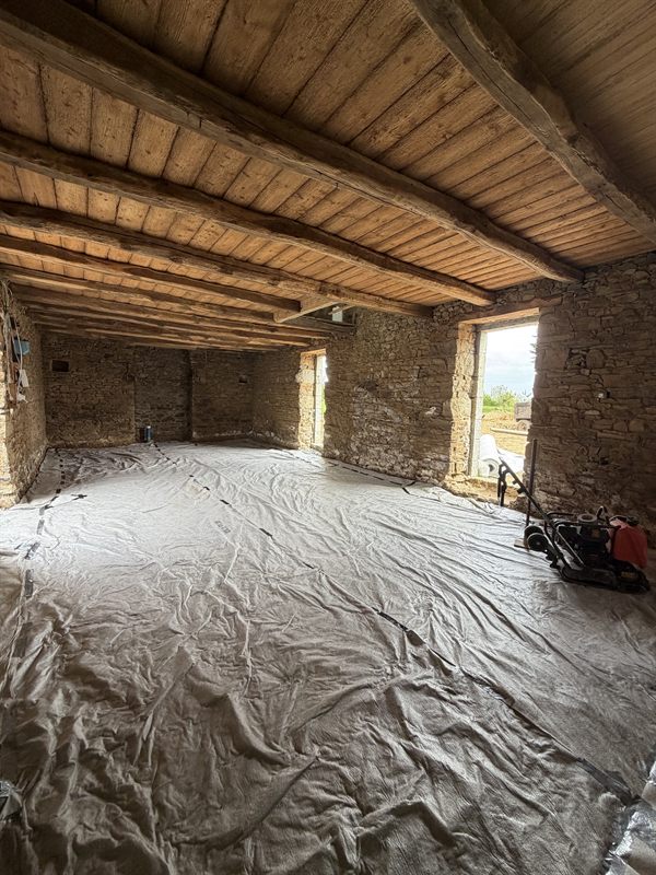 Salle en pierre à plafond bois, sol protégé par un géotextile, plaque vibrante