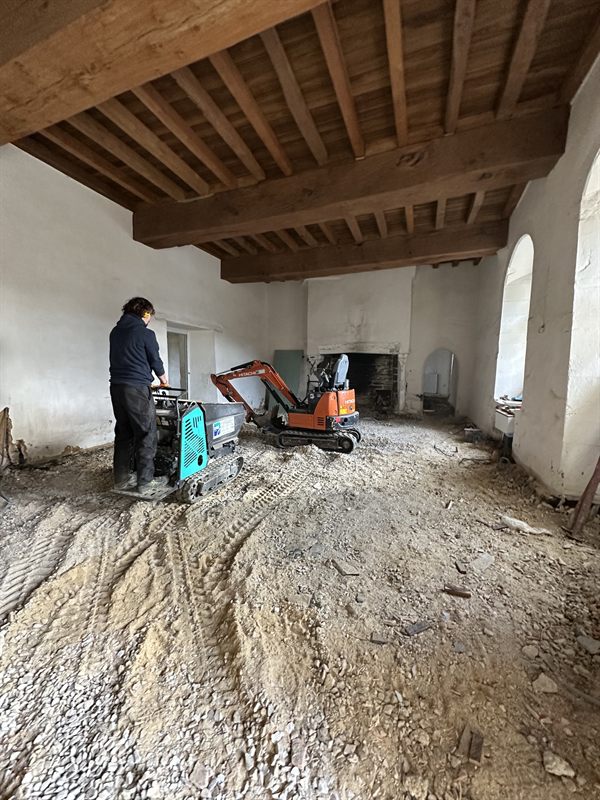 Dumper à chenilles et pelle dans une pièce en rénovation avec cheminée en pierre