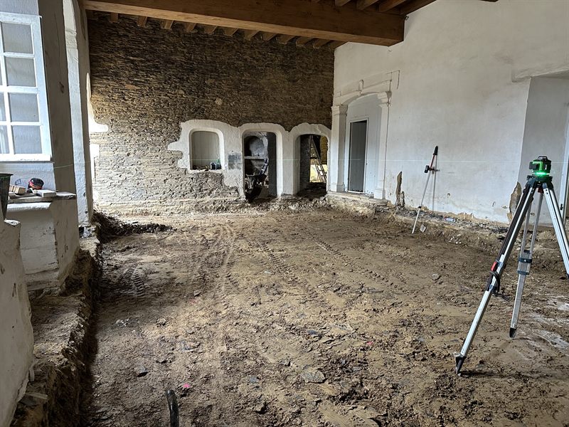 Sol intérieur décaissé, niveau laser sur trépied, mur en pierre à niches cintrées