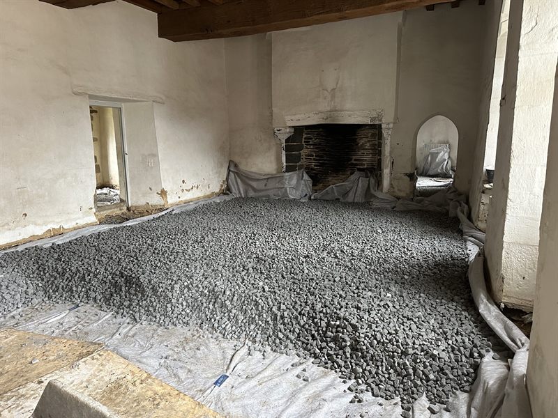 Pièce en pierre avec grande cheminée, sol recouvert de pierres concassées sur géotextile